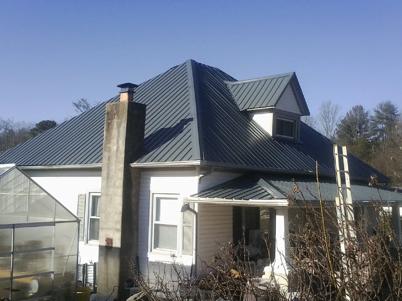 Dark blue standing seam metal roof on a white farmhouse with dormer — Slate & Tile Roof Repair by Roofing Brothers in Branchdale