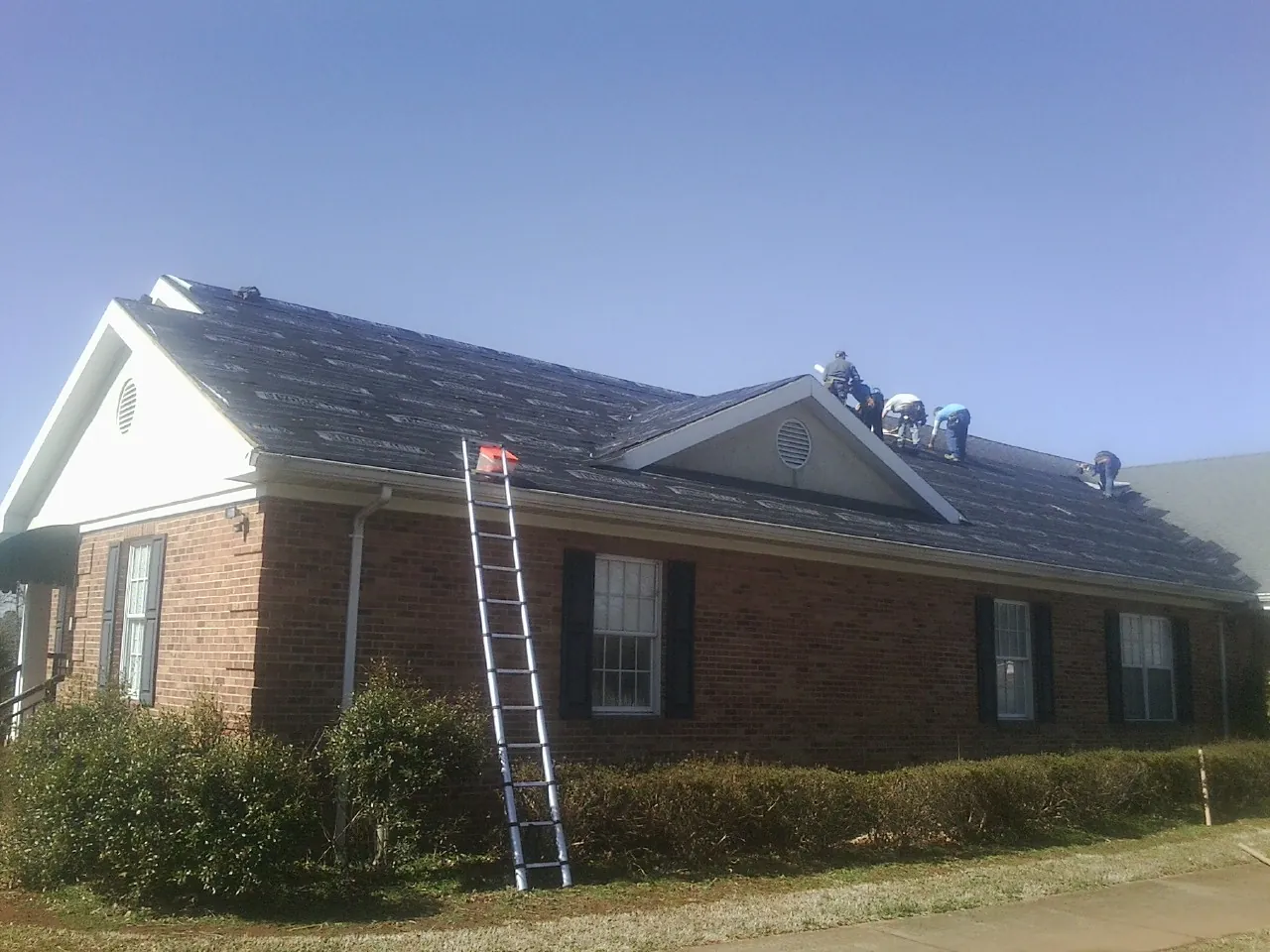 Crew tearing shingles off a brick ranch roof with a ladder set — Emergency Roof Repair work by our crew in Branchdale