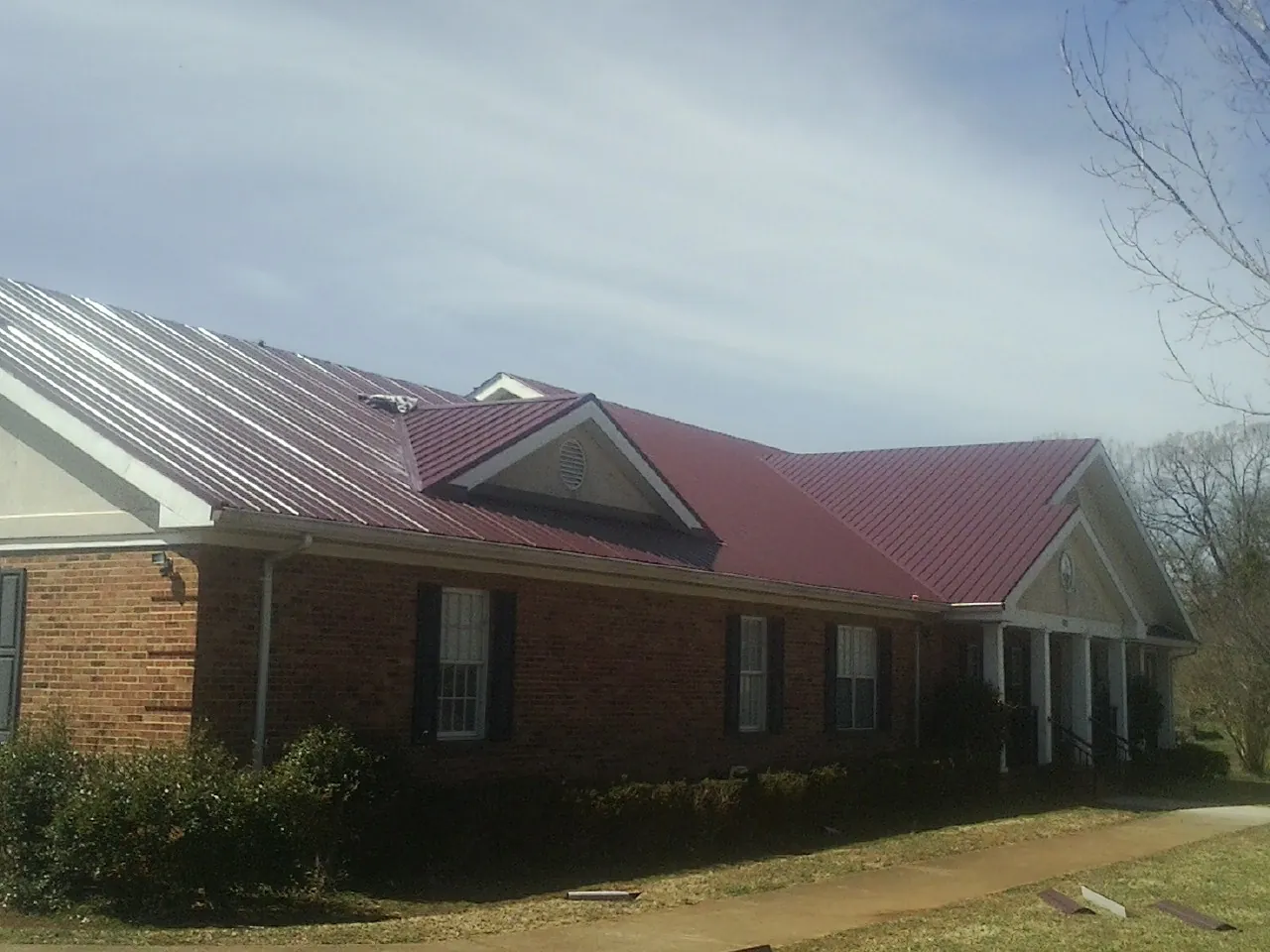 Red metal roof with gabled entries on a long brick building, from a Hail Damage Roof Repair job in Branchdale