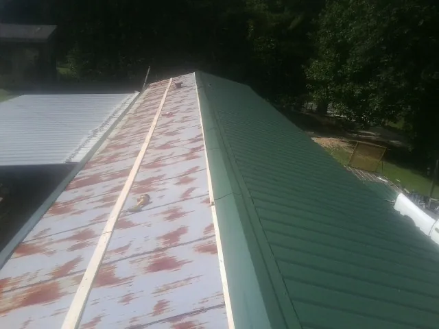 Old rusted panels beside newly installed green metal roofing — Wind Damage Roof Repair by Roofing Brothers in Branchdale