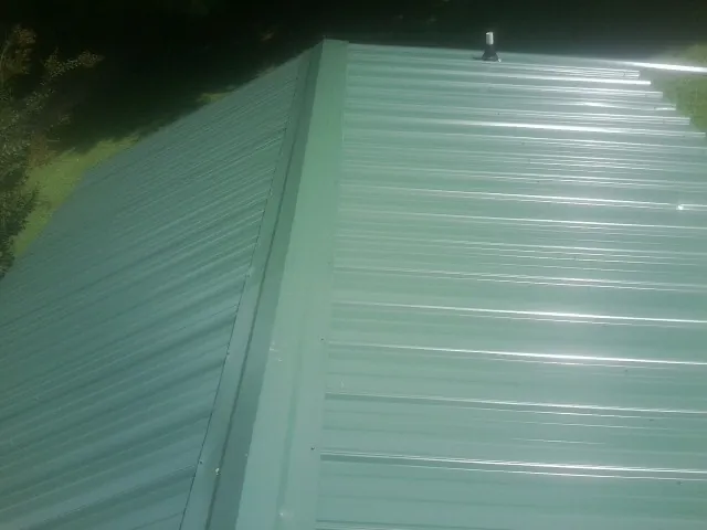 New green metal panels meeting at the ridge of a roof — Flat Roof Repair work by our crew in Branchdale