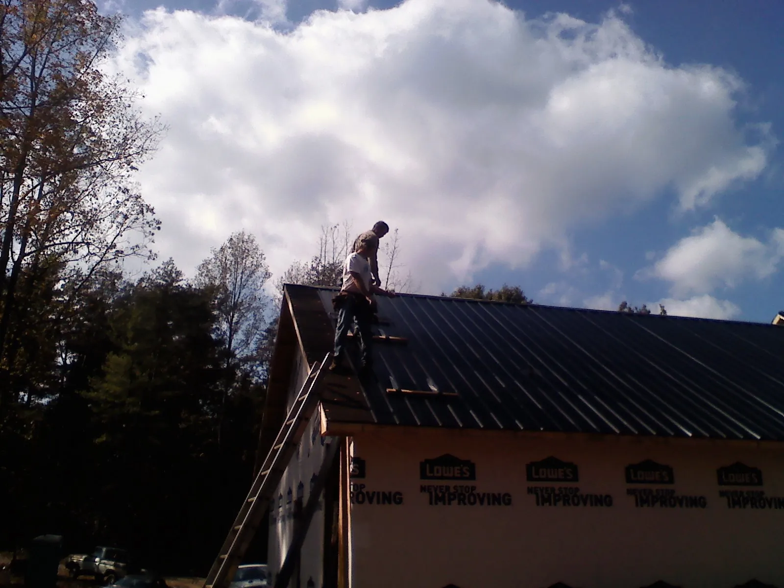 Roofer fastening dark metal panels high against a cloudy sky, from a Roof Inspection job in Branchdale