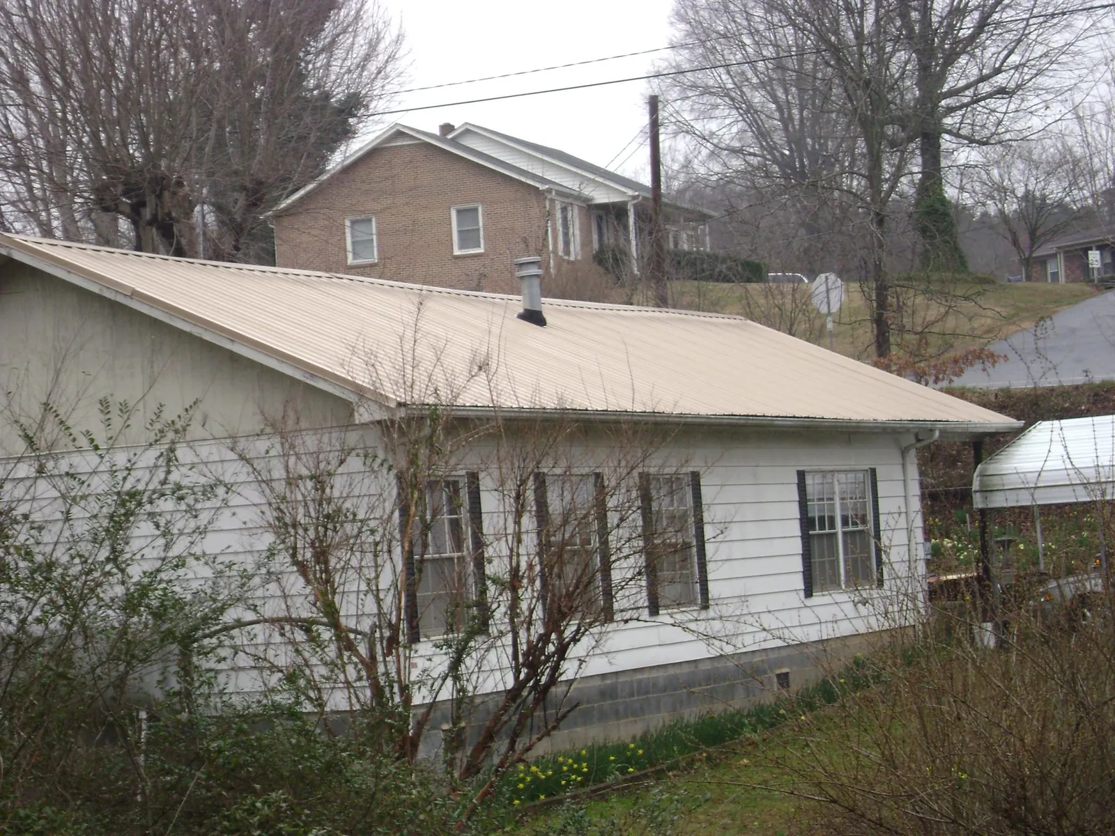 Tan metal roof on a white sided house set into a hillside — Commercial Roofing by Roofing Brothers in Branchdale