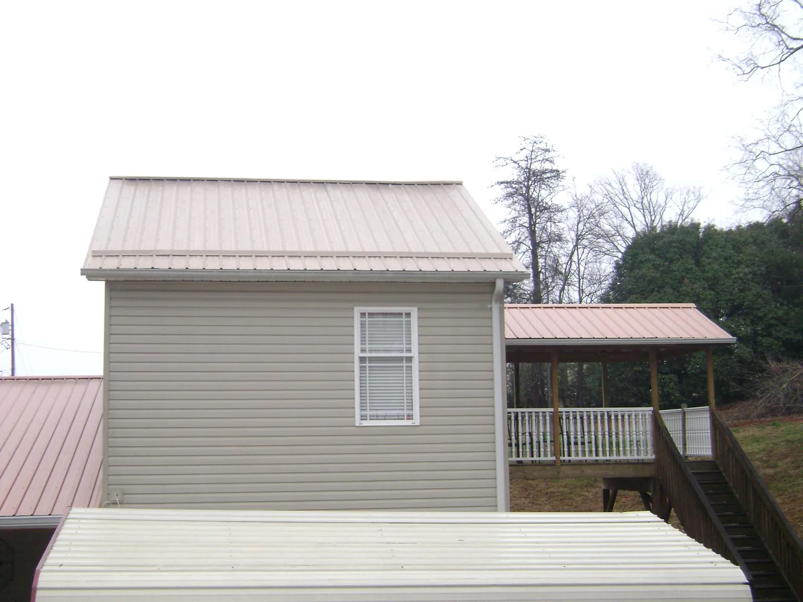 Tan metal roofs on a two story addition and attached porch, from a Roof Replacement job in Branchdale